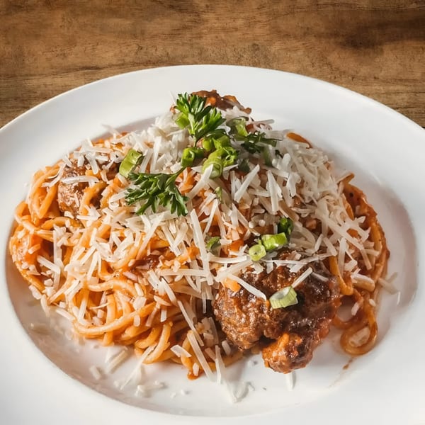 Spaghetti with meatballs, tomato sauce, shredded Parmesan cheese, and fresh herbs on a white plate.