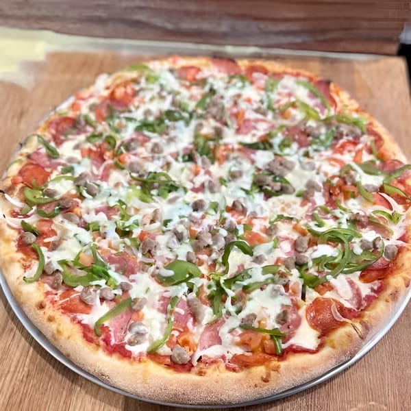 A whole pizza with pepperoni, sausage, green peppers, and a white sauce drizzle.