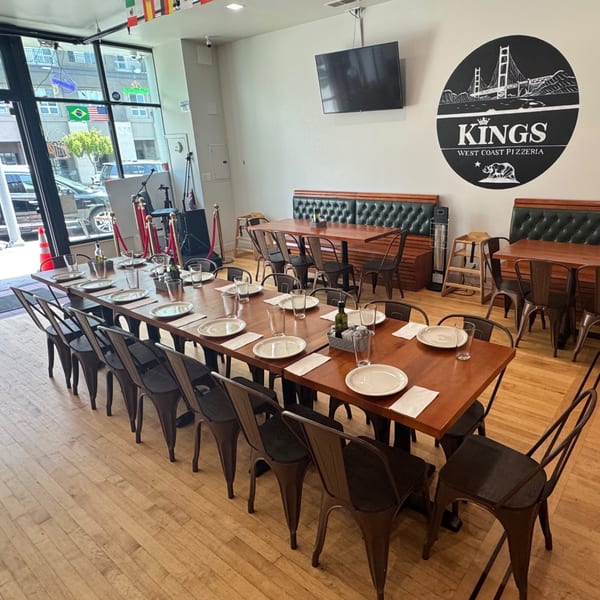 Kings West Coast Pizzeria dining room with long communal table, booth seating, and large logo on the wall.