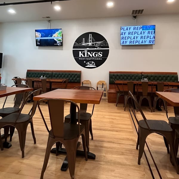 Interior of Kings West Coast Pizzeria with tables, chairs, booths, and the restaurant logo on the wall.
