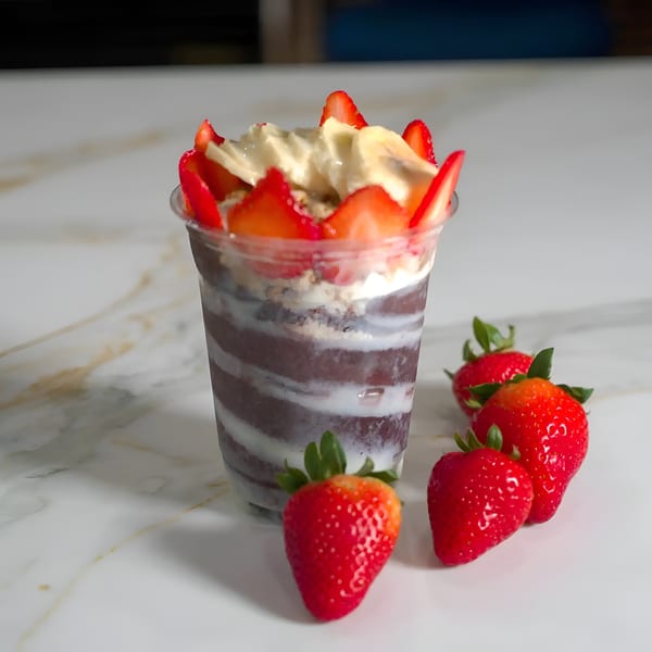 A clear cup of acai with white stripes, topped with strawberries, bananas, and granola.