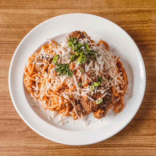 Spaghetti and meatballs topped with shredded cheese, parsley, and green onions on a white plate.