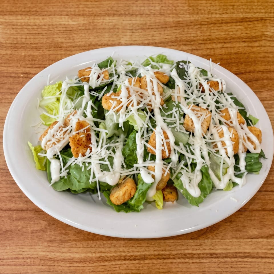Caesar salad with green lettuce, croutons, white dressing, and shredded cheese on a white plate.