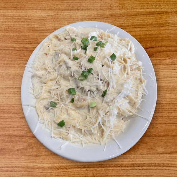 Creamy pasta dish topped with shredded Parmesan cheese and chopped green onions on a white plate.