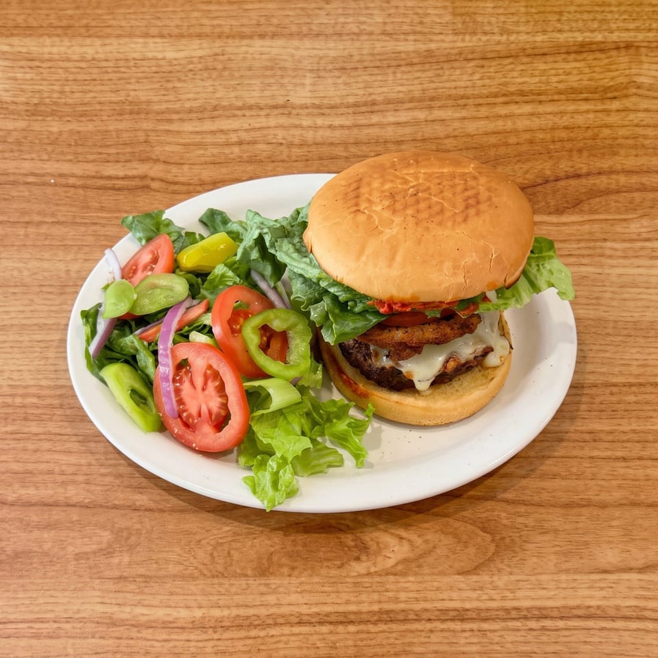 A cheeseburger with fried onions and a side salad with tomatoes, peppers, and onions.